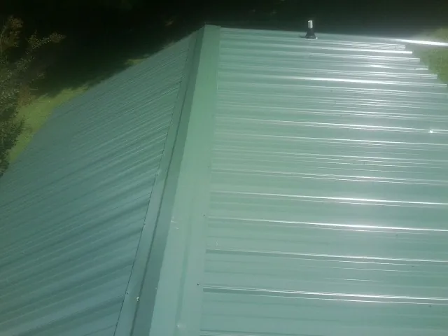 New green metal panels meeting at the ridge of a roof — Flat Roof Repair work by our crew in Belton